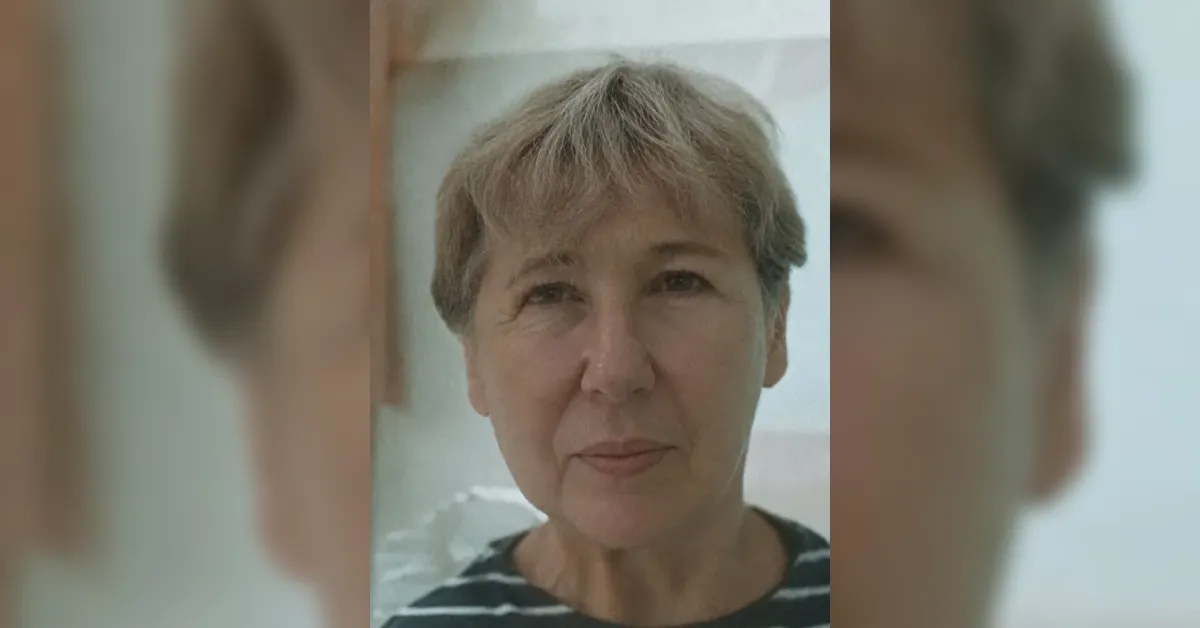 Portrait of a middle-aged woman with short gray hair, wearing a black-and-white striped shirt, looking at the camera with a neutral expression.