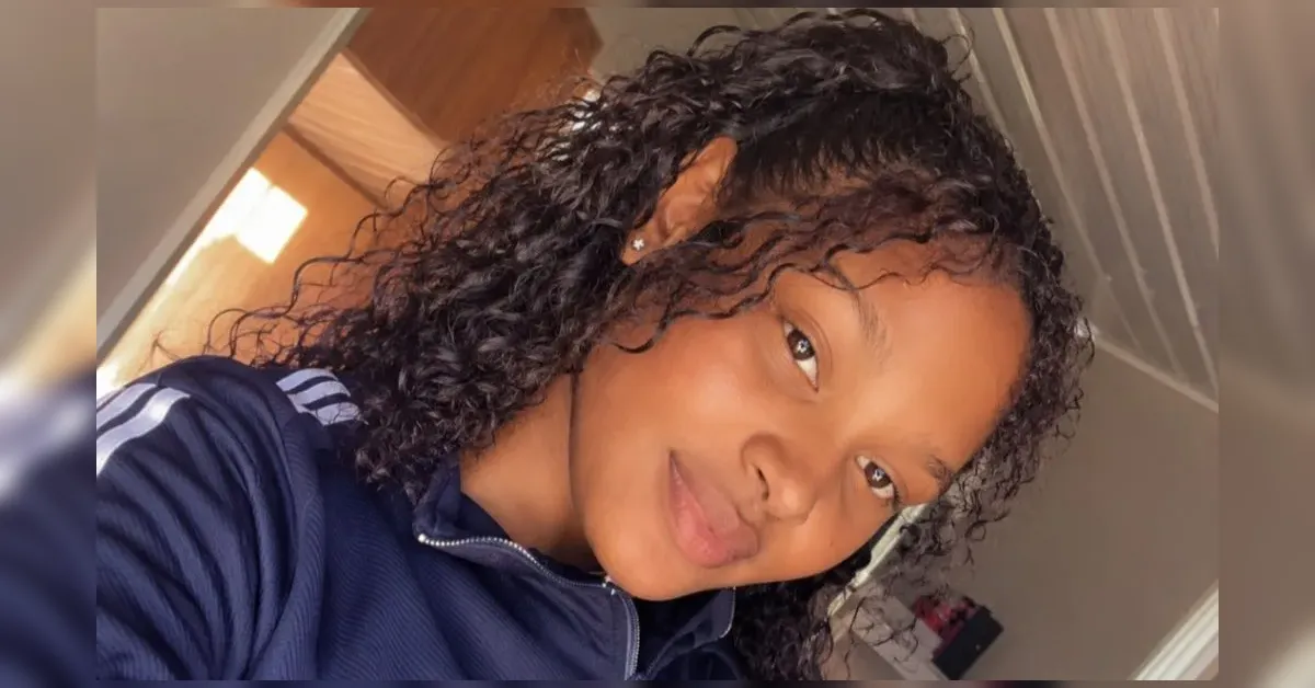 Young woman with curly, damp hair wearing a navy zip-up jacket, taking a selfie indoors with a soft smile on her face.