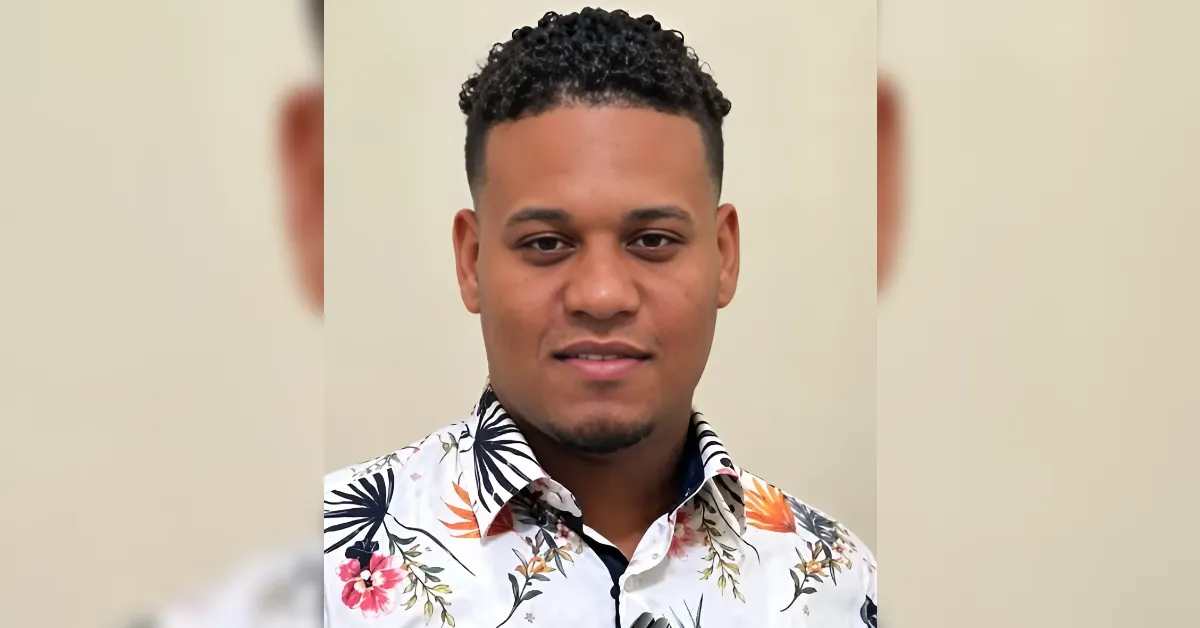 Head-and-shoulders portrait of a man with short curly hair wearing a white floral shirt, looking at the camera.