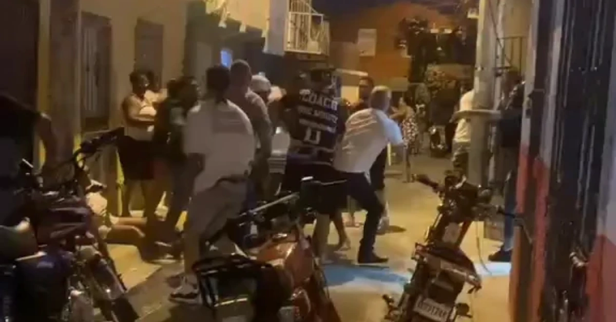 Nighttime street scene with a crowd gathered around parked motorcycles, conversing among themselves.