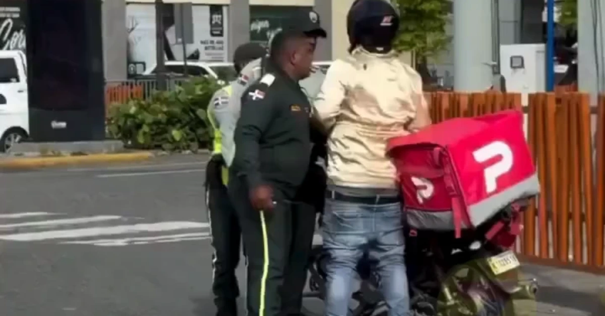 Two men in uniforms talk to a rider beside a red courier motorcycle on a city street.