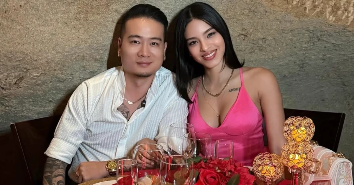 Smiling couple sits at a table with wine glasses, red roses, and warm candlelight decorations behind them on a dining date scene.