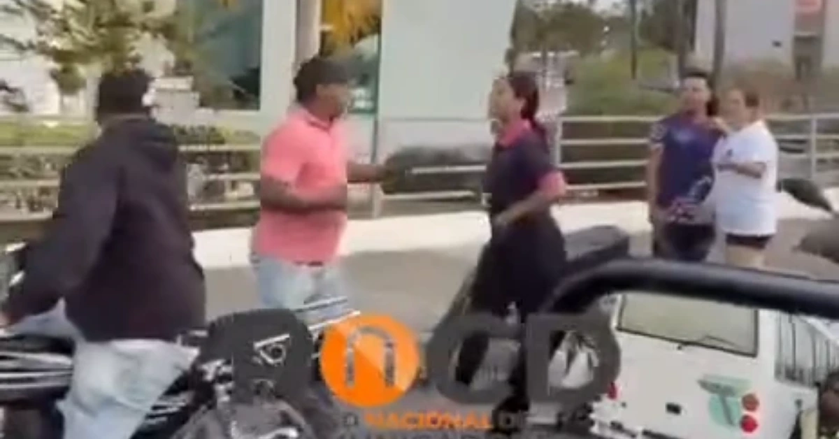 Two men argue on a sidewalk beside a parked car while bystanders watch.