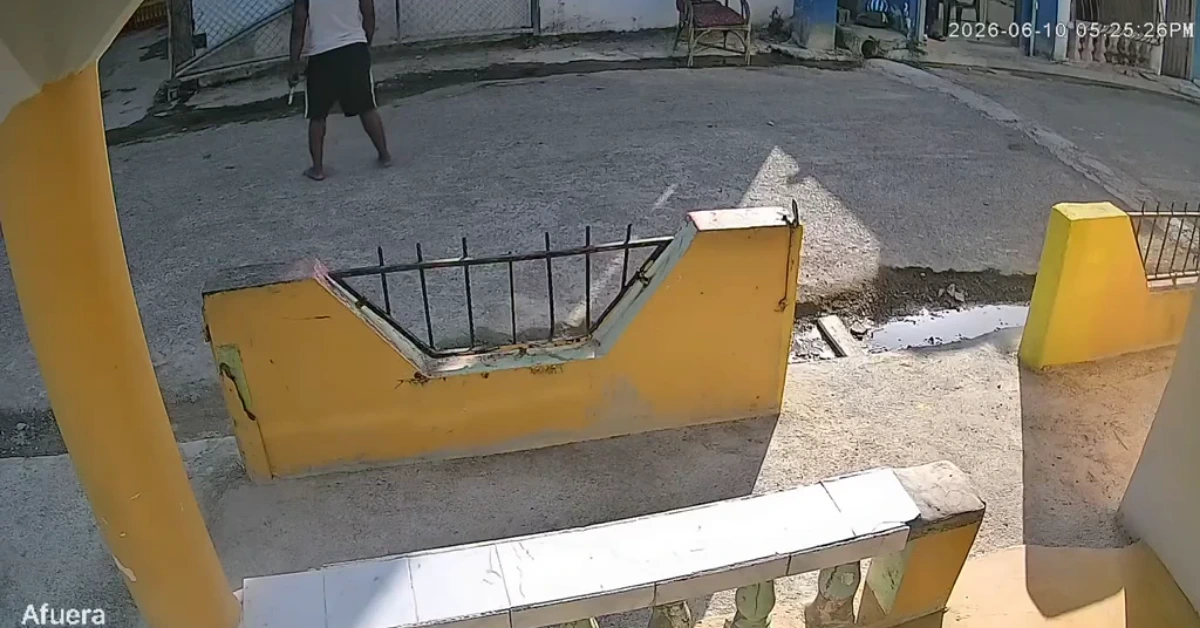Surveillance still of a yellow concrete barrier and steps in the foreground with a man walking on a gravel lot in the background; timestamp visible.