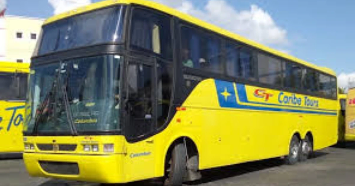 Bright yellow tour bus with a blue stripe and star logo parked outdoors in a sunny setting, front view.