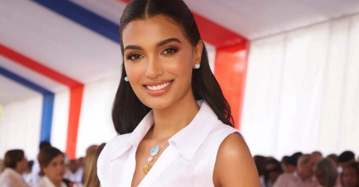 Smiling woman in a white sleeveless blouse at an event with red, white, and blue decor in the background.