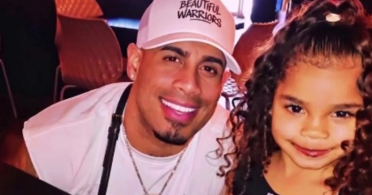 Man in a white shirt and cap smiling beside a young girl with curly hair, both looking at the camera.