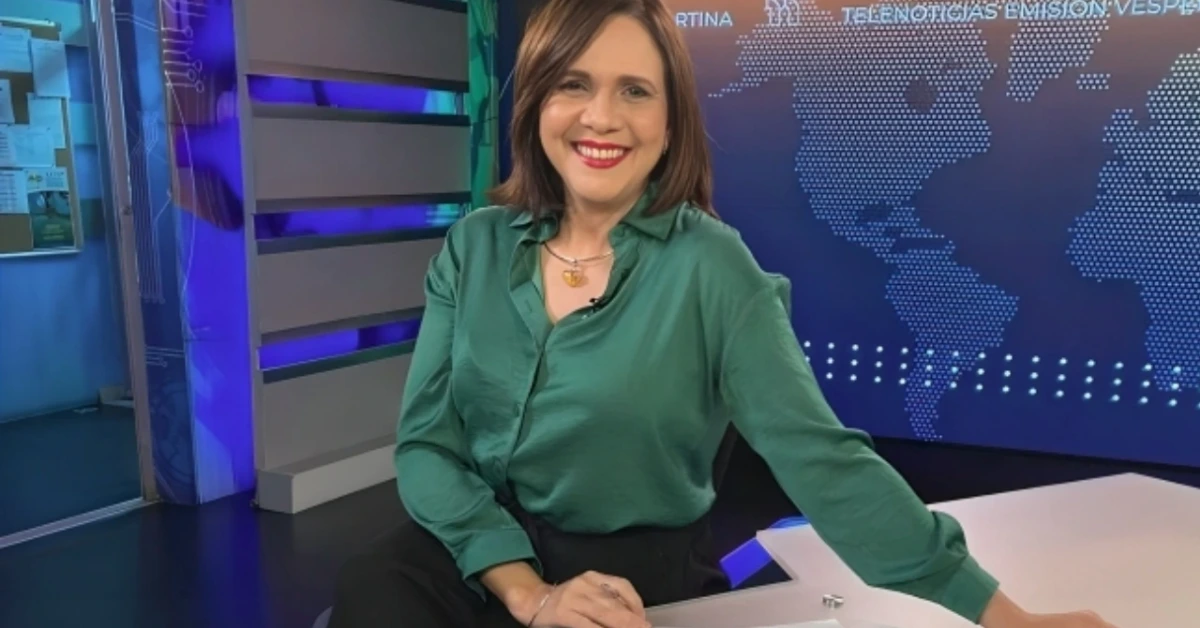Female news anchor in a green blouse sits at a desk in a TV studio with a world map backdrop and blue lighting.
