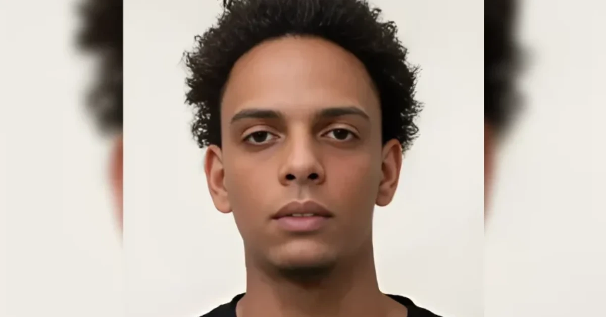 Close-up portrait of a young man with short curly hair against a pale background, looking straight ahead.