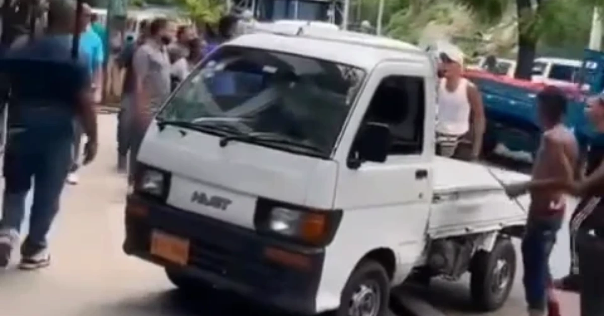 White mini pickup truck on a crowded street with bystanders gathered around it