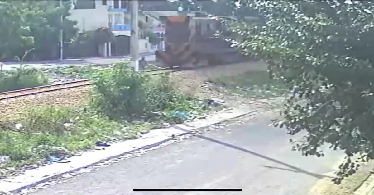 Armored military vehicle on a street beside railroad tracks, with overgrown vegetation and residential buildings in the background.