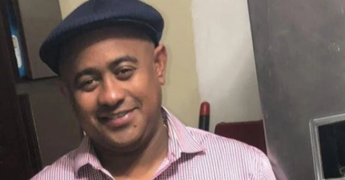 Smiling man wearing a dark flat cap and pink striped shirt indoors, facing the camera.