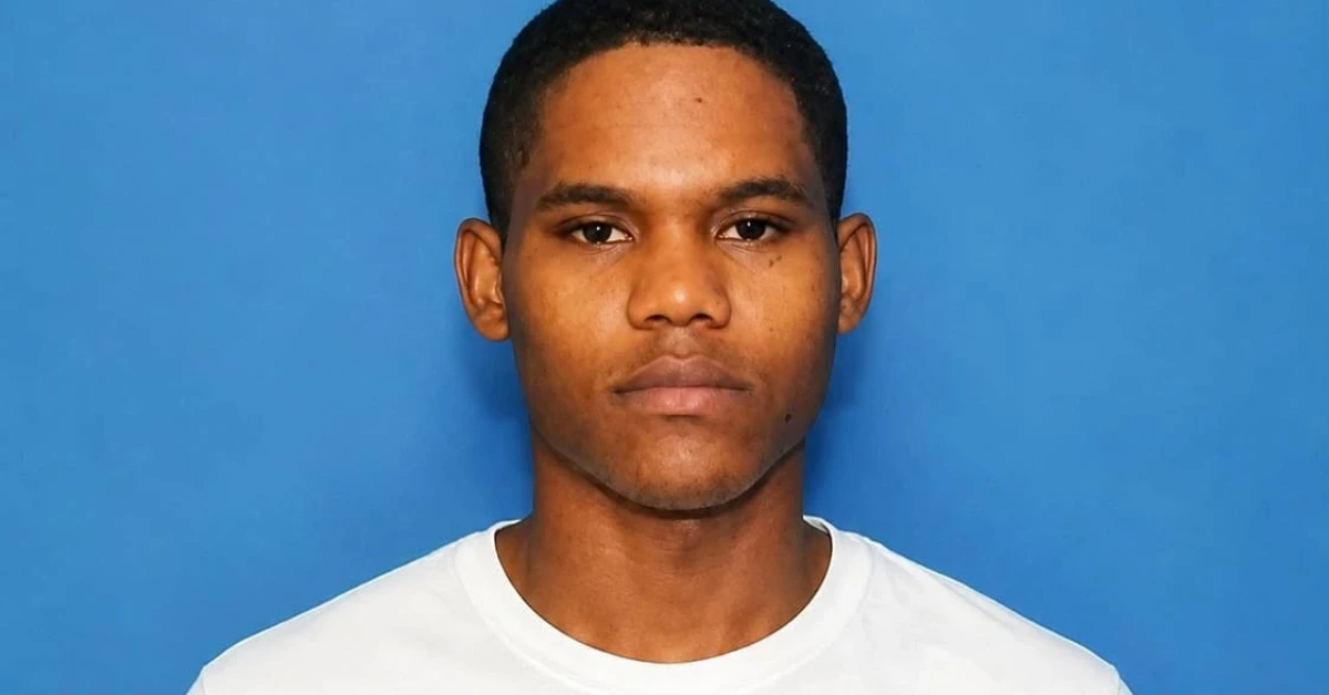 Young man with short hair in a white T-shirt against a blue backdrop, neutral expression.