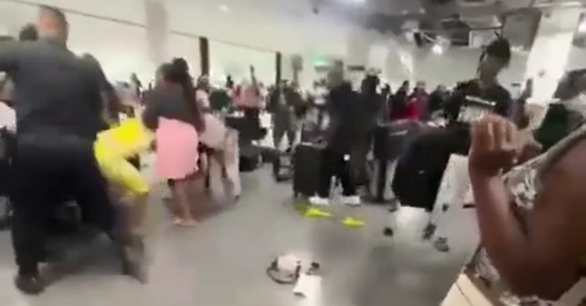 Crowded indoor terminal or hall with many people pushing through, luggage scattered on the floor, conveying a chaotic scene.