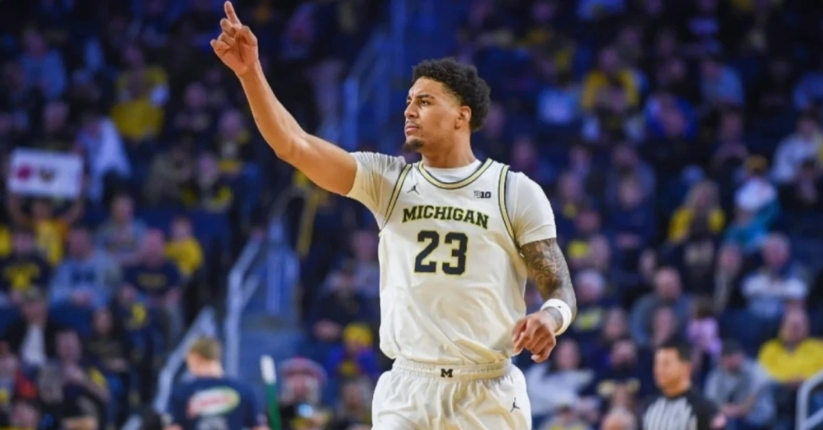 Michigan basketball player wearing jersey number 23 raises his right arm upward on the court during a game.