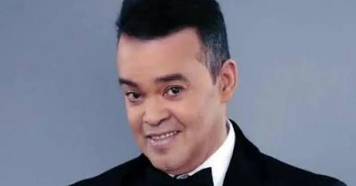 Smiling man in a black tuxedo and bow tie against a gray studio background.