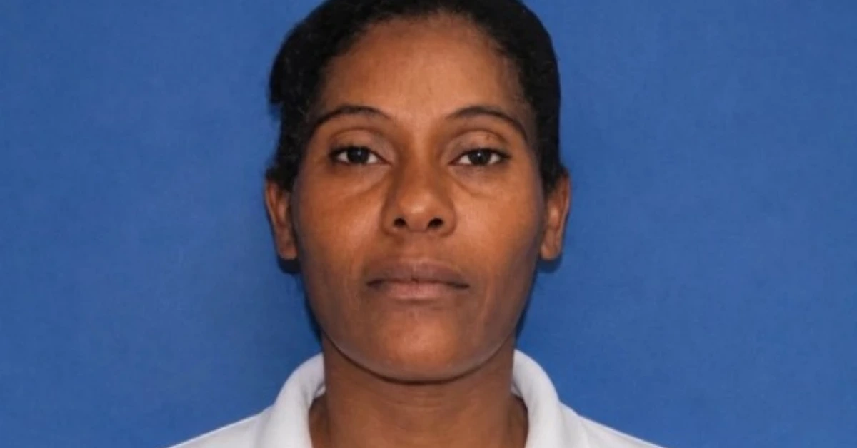 Head-and-shoulders portrait of a woman with dark hair and a neutral expression against a blue background, wearing a white collared shirt (ID/photo for records)