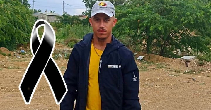 Man standing outdoors in a yellow shirt and dark jacket with a large black awareness ribbon graphic beside him.