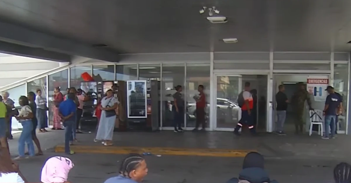 People waiting outside a glass-front building entrance, with an emergency area visible on the right.