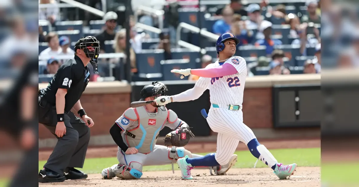 Baseball batter in a white pinstripe uniform swings at a pitch as catcher crouches behind home plate and umpire watches, with fans in the stands in the background.
