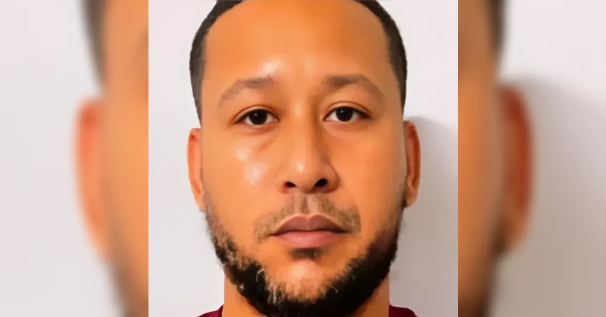 Close-up of a man with a short beard and mustache, wearing a maroon shirt, looking straight at the camera against a white background.