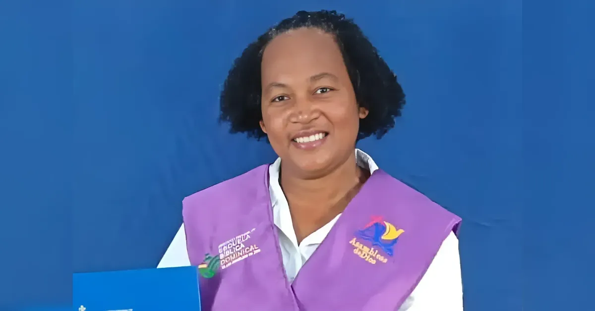 Smiling woman wearing a purple vest over a white shirt, holding a blue certificate folder, posed against a blue backdrop.
