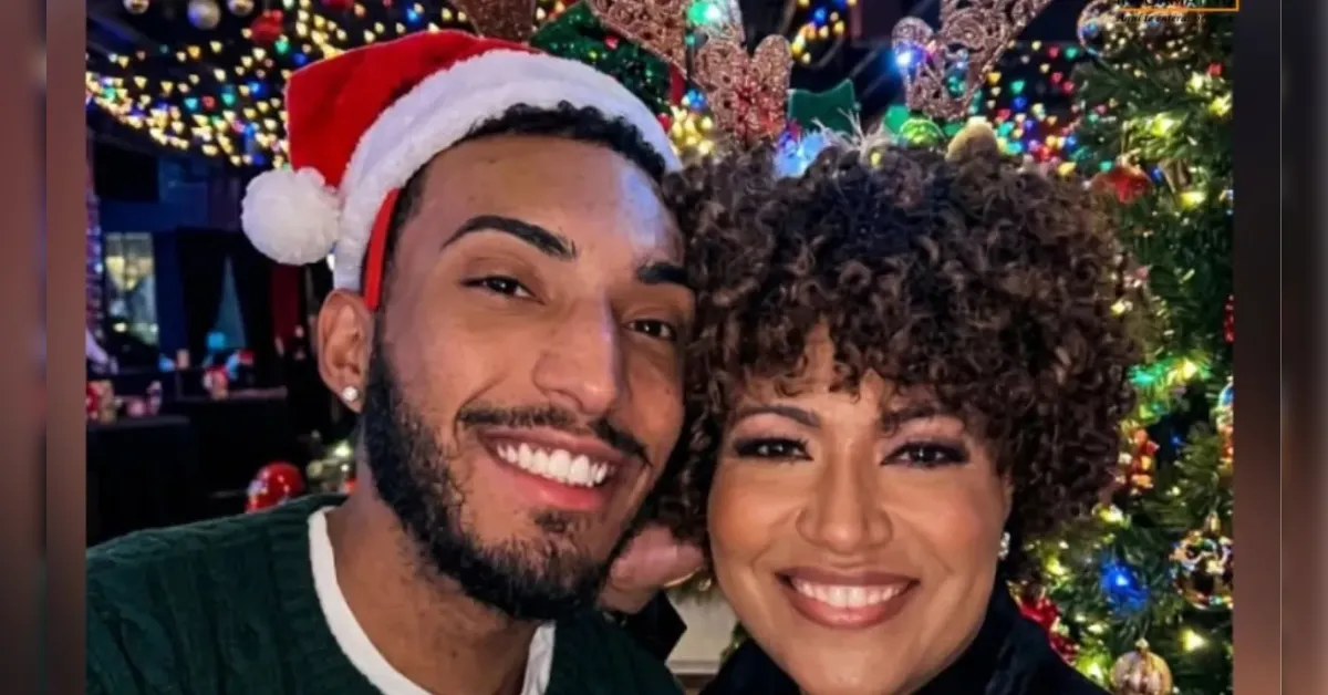 Two people smiling for a selfie at a festive Christmas display with colorful lights and a decorated tree in the background.