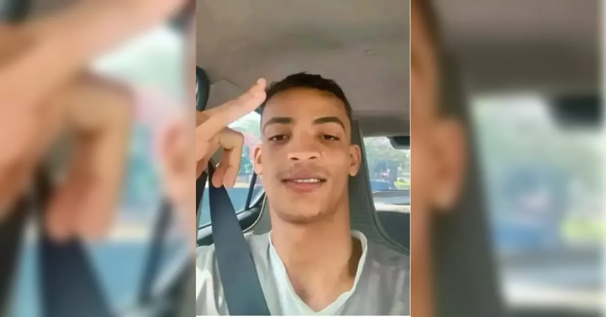 Young man wearing a seatbelt in a car, smiling at the camera and making a peace sign near his head.