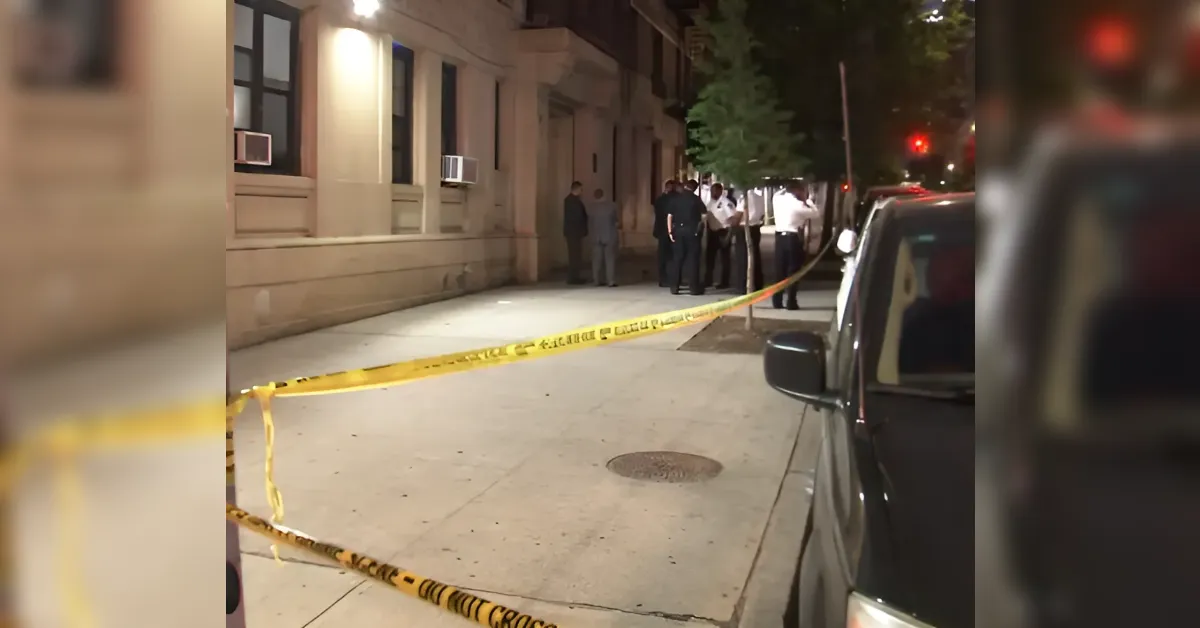 Nighttime street with yellow crime-scene tape, a small group near a beige building, and a parked car on the right.