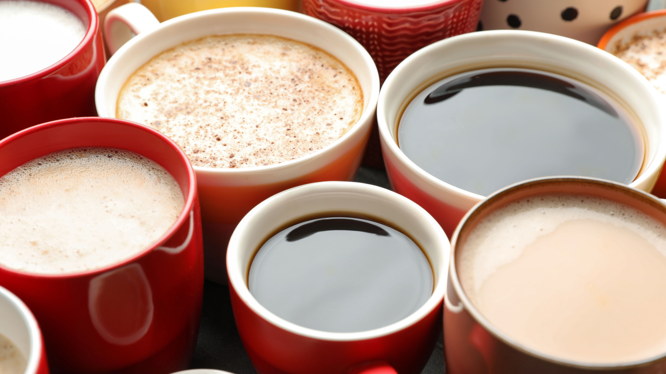 Top-down view of red cups filled with different coffees: black coffee, latte, cappuccino, and milk coffee in a sunny arrangement