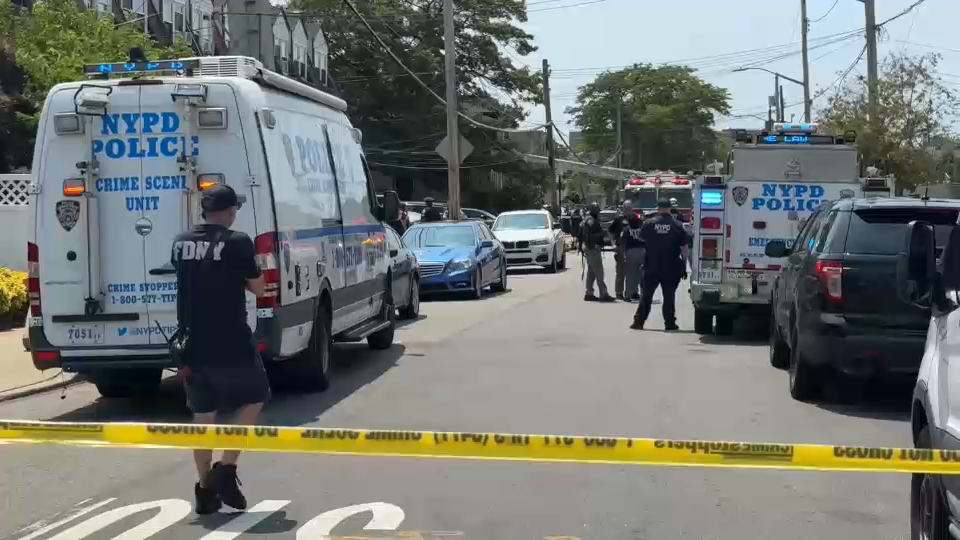 NYPD crime-scene with police vans and officers blocking a city street, yellow caution tape across the road.