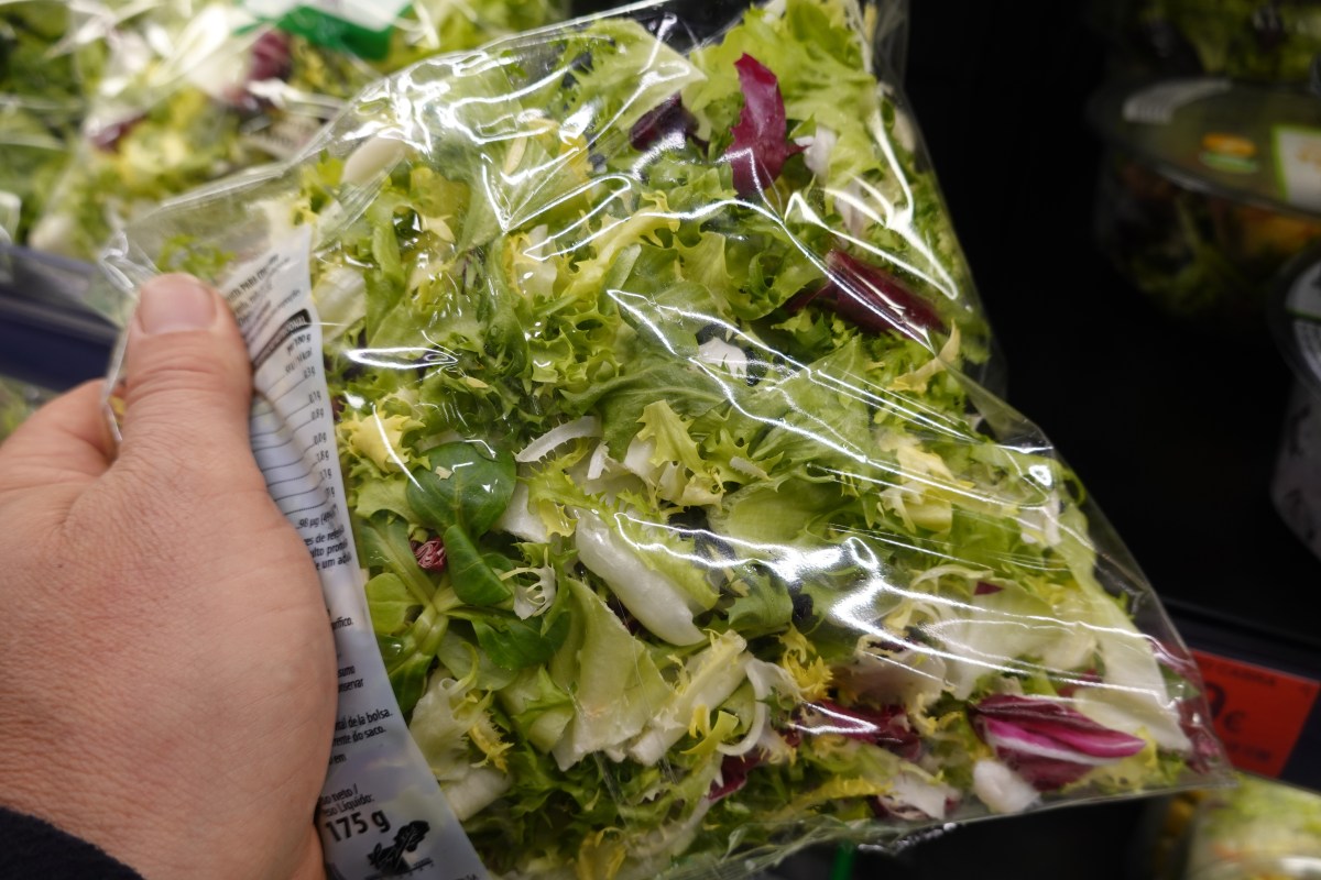 Person holding a sealed bag of mixed green salad in a supermarket.