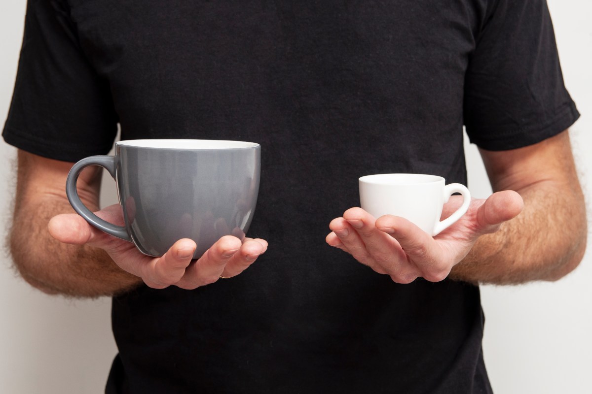 Person in a black shirt holds a large gray mug in one hand and a small white espresso cup in the other.