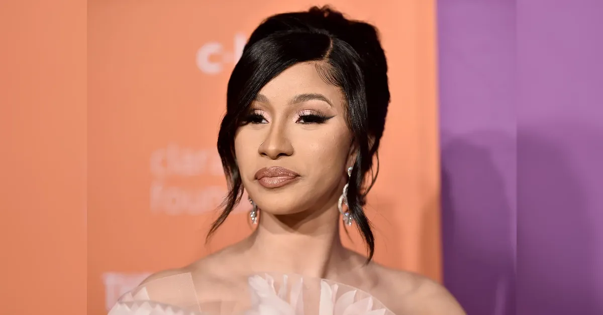 Portrait of a woman with dark hair and statement earrings at a red-carpet backdrop (orange and purple background).