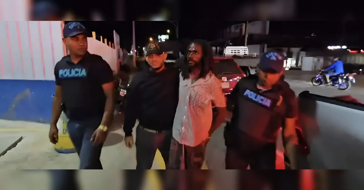Nighttime street scene with two police officers escorting a man in a striped shirt; a third officer watches, with a motorcycle in the background.