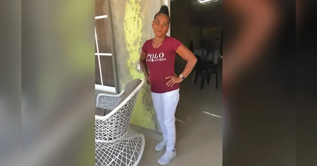 Woman standing with hands on hips on a porch, wearing a maroon polo shirt, white pants, and sneakers beside a wicker chair.