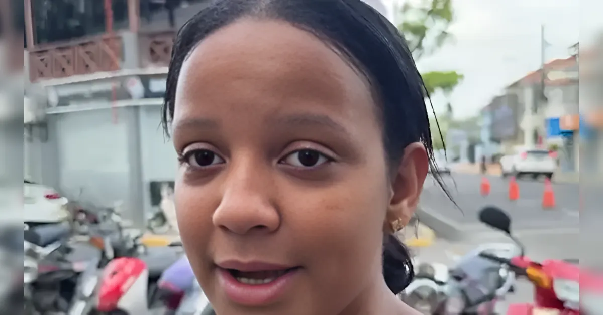Close-up of a woman speaking outdoors on a street with parked motorcycles and orange traffic cones in the background.