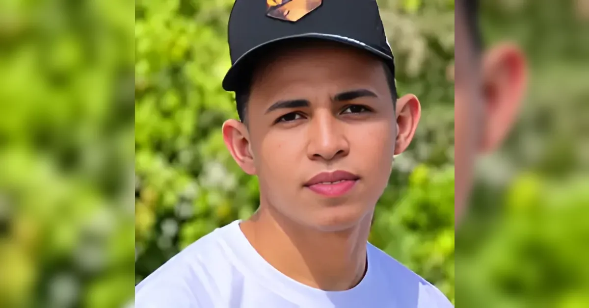 Portrait of a young man outdoors wearing a black cap and white shirt, looking at the camera with a neutral expression.