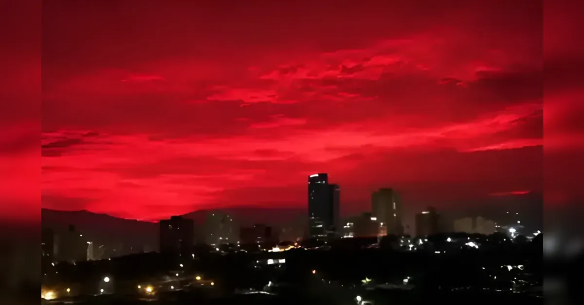 City skyline at dusk with a bright red sunset staining the sky over dark buildings and city lights.
