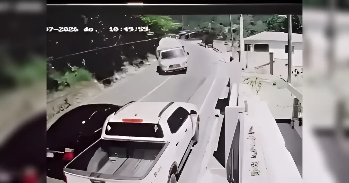 Security camera frame of a white pickup truck driving on a curved hillside street, with a dark car parked on the left and a barrier on the right.