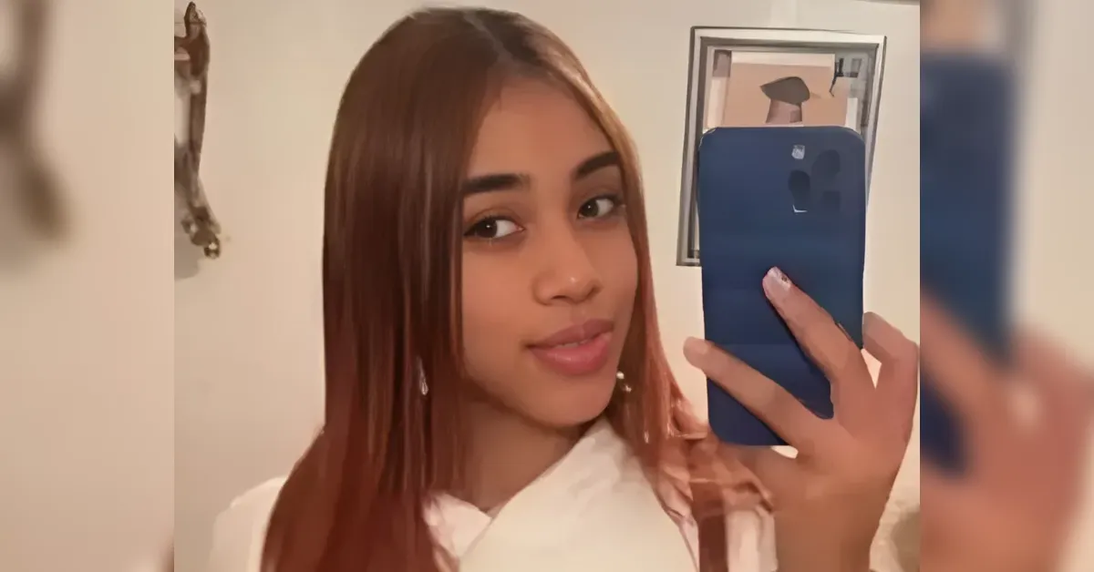 Young woman with long brown hair wearing a white top takes a mirror selfie holding a blue smartphone.