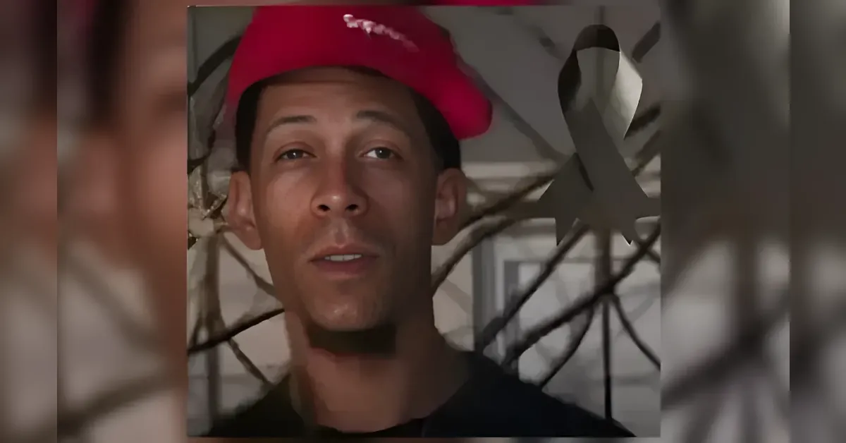 Portrait of a man wearing a red cap, facing the camera, with a blurred plant-like background.