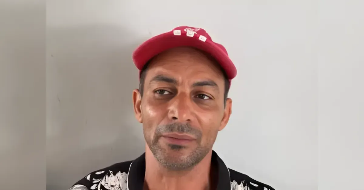 Man wearing a red cap and black floral shirt, looking slightly to the right.