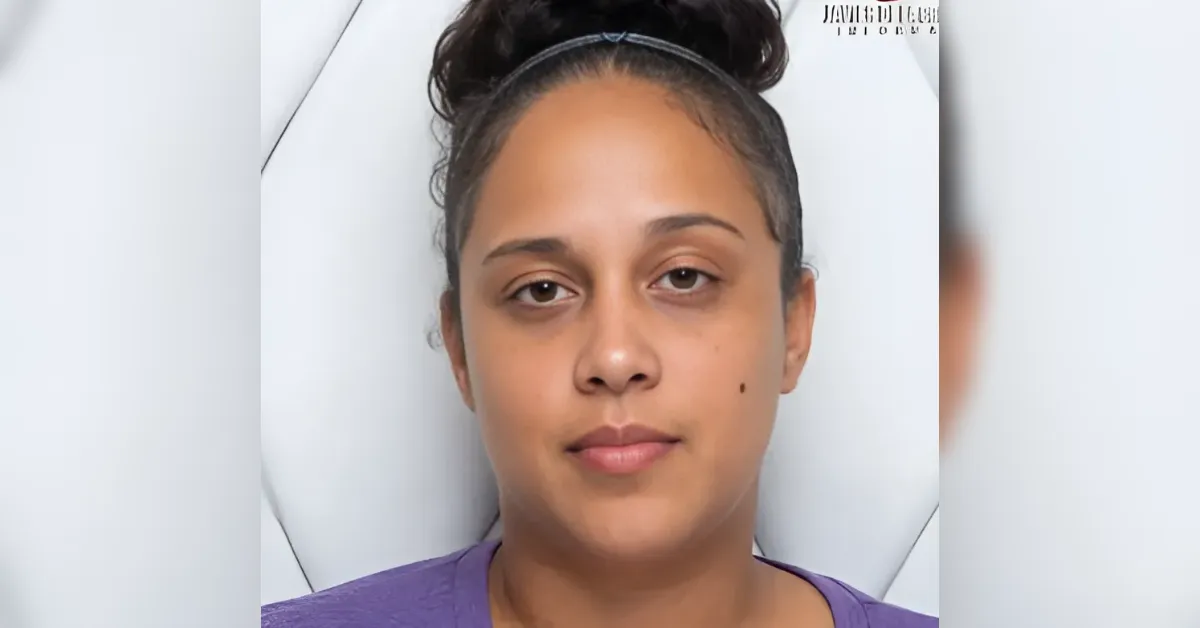 Close-up of a woman with a bun and headband lying down, wearing a purple shirt, with a neutral expression and a small mole on her right cheek.