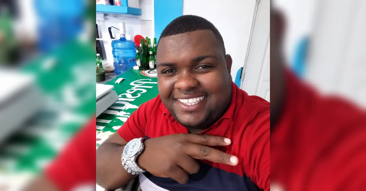Smiling man in a red polo shirt posing for a selfie in a shop, wearing a large silver wristwatch.
