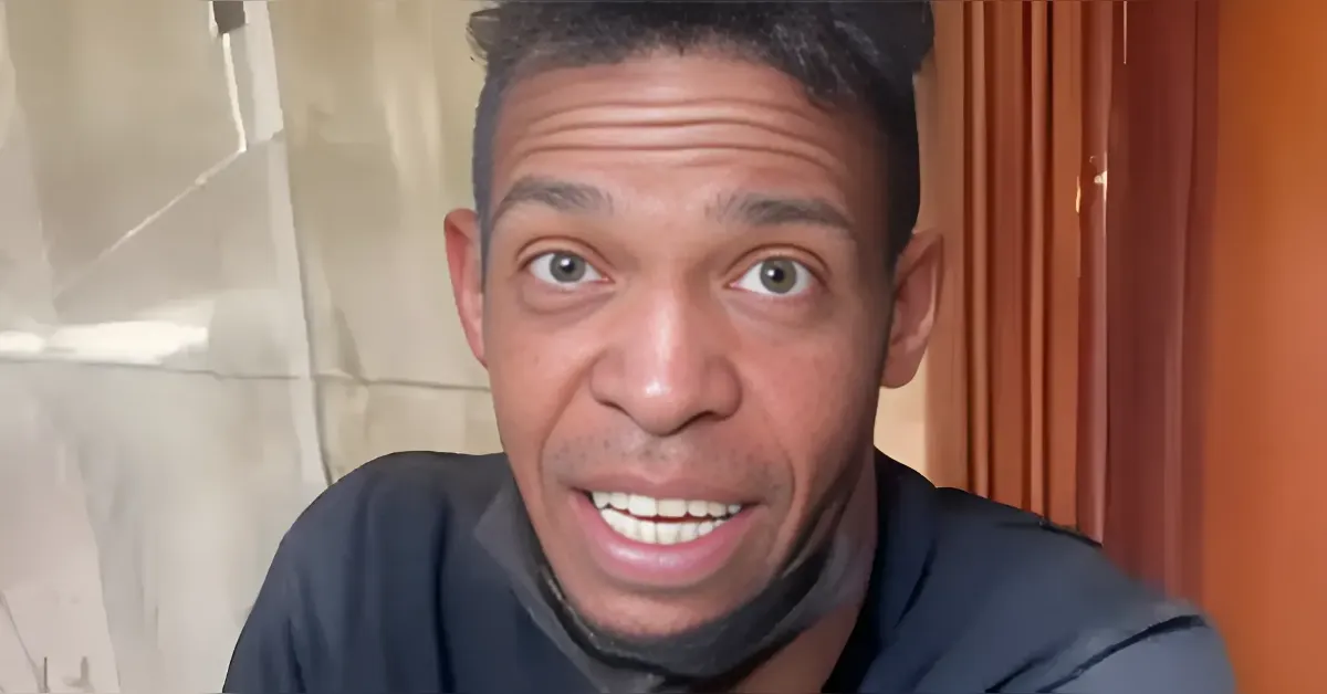 Close-up of a man facing the camera with wide eyes and mouth open, wearing a dark shirt and with a mask under his chin.