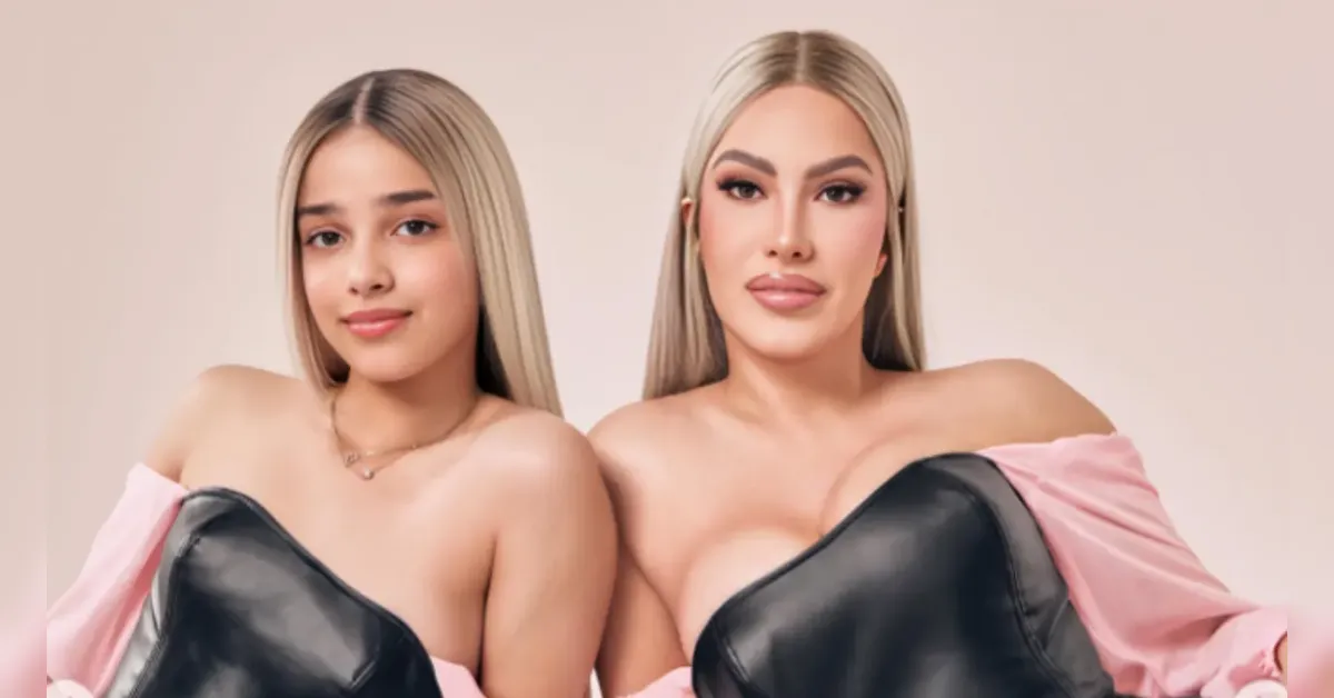 Two young women with long blonde hair posing side by side in pink off-shoulder outfits with black leather accents, smiling at the camera.