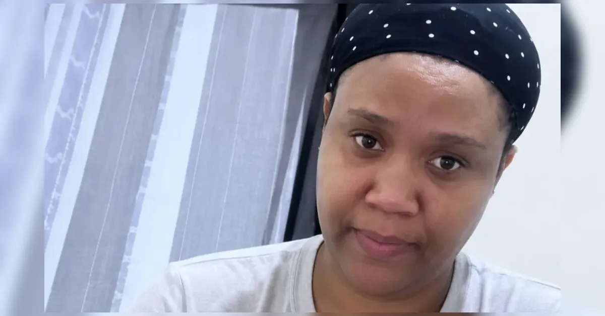 Close-up portrait of a woman wearing a black polka-dot headscarf, looking at the camera in a neutral expression.