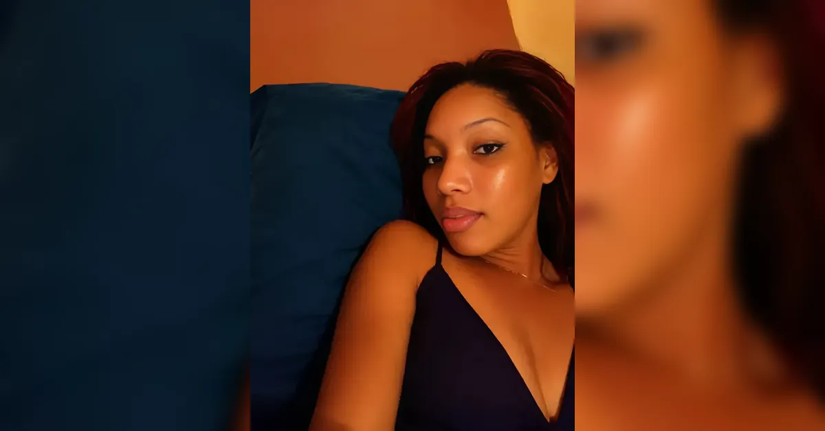 Woman lying on a blue pillow, wearing a black top, looking toward the camera with a relaxed expression.