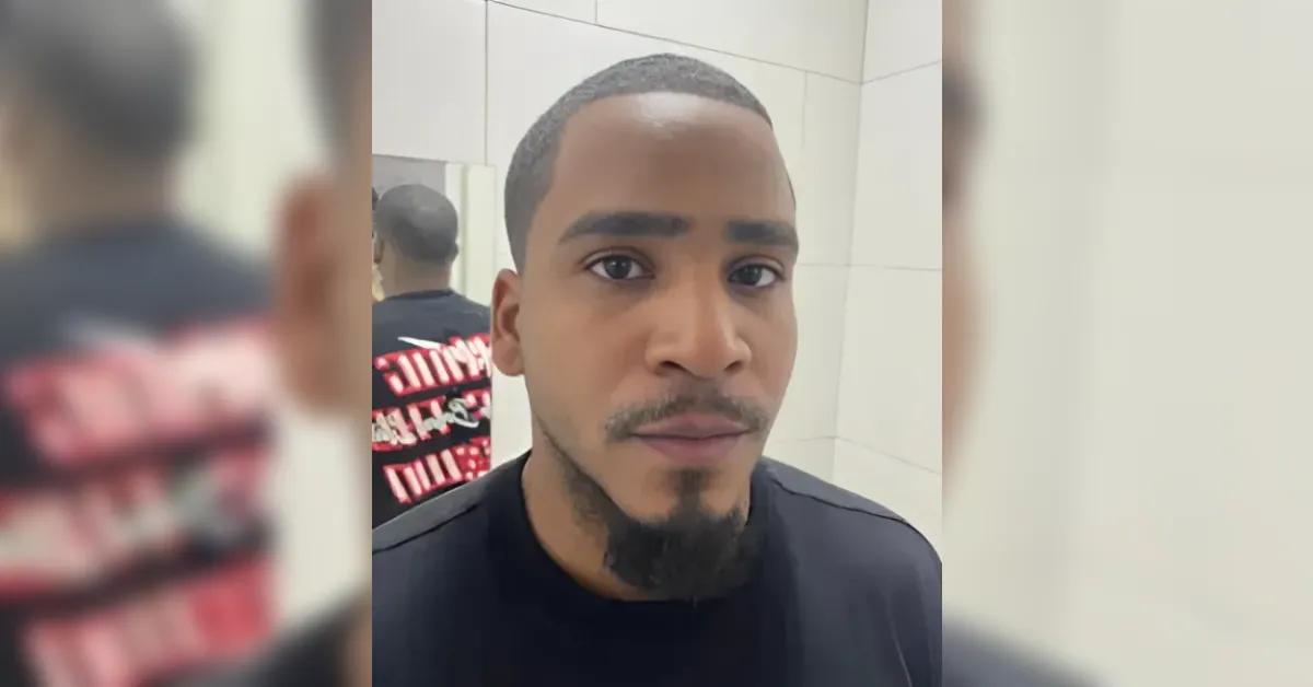 Close-up of a young man with a buzzed haircut and goatee taking a selfie in a tiled bathroom mirror.